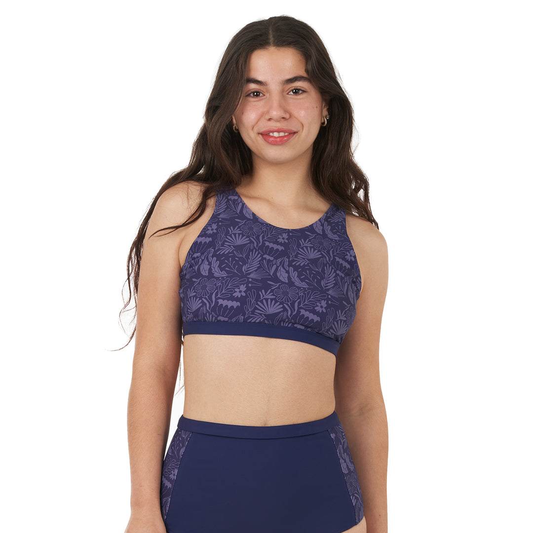 A woman wearing a high neck bikini top with a halter shape and a keyhole back detail. The top is navy with a floral pattern and includes adjustable straps and padded removable cups.