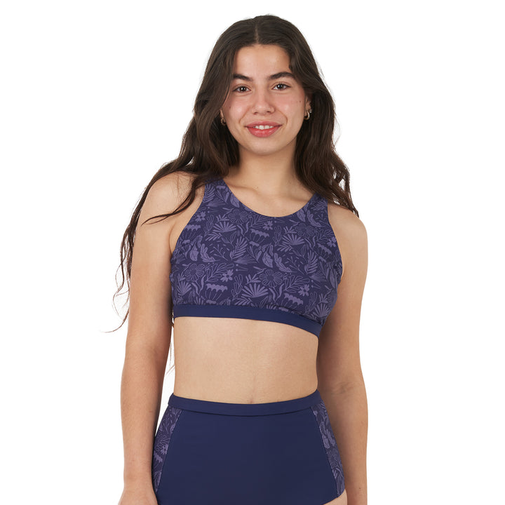 A woman wearing a high neck bikini top with a halter shape and a keyhole back detail. The top is navy with a floral pattern and includes adjustable straps and padded removable cups.